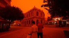 Люди идут сквозь туман, образовавшийся из-за песчаной пыли из Сахары, принесенной сильными южными ветрами, в Ираклионе на острове Крит, 1 апреля 2026 года.