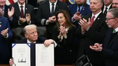 Trump imzaladığı anlaşmayı çevresine gösteriyor. 