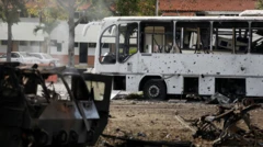 Un autobus blanco y otro vehículo, uno militar, seriamente dañados