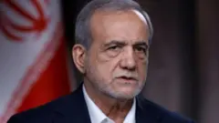 الرئيس الإيراني يرتدي بدلة سوداء وقميص أبيض وخلفه علم إيران 