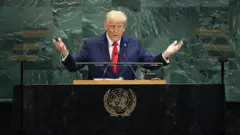 Donald Trump, com as mãos espalmadas e os braços abertos, gravata vermelha e terno azul escuro, discursando no púlpito da Assembleia Geral da ONU