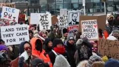 防寒具に身を包んだ人々がプラカードを持って更新している。J・D・ヴァンス副大統領の似顔絵の下に「BETA」と書いたプラカードを持っている人もいる