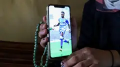 أرملة لاعب كرة القدم سليمان العبيد، المعروف باسم "بيليه الفلسطيني" تعرض صورة له على هاتف محمول داخل خيمتهم في مدينة غزة