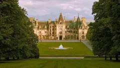 Vista panorámica de la mansión Biltmore que se ve tras un gran jardín con árboles y una fuente en el centro  