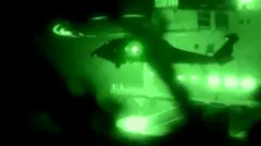A helicopter hovers in front of a ship in footage shot at night