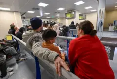 Família sentada em sala de espera, incluindo uma criança, todos de costas