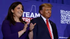 Elise Stefanik usa um vestido azul e bate palmas. Ela estámelhor site de dicas de apostaspémelhor site de dicas de apostasum palco ao ladomelhor site de dicas de apostasDonald Trump, que usa um terno escuro e gravata vermelha