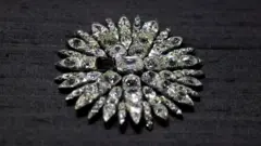 Joia deslumbrante, incrustada com diamantes em forma de sol, sobre um fundo preto. A peça que falta indica o centro da peça.