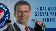 İmamoğlu'nun büyük bir outdoor görselinin önünde şemsiyeli bir kadın ve bir başka kadın geçiyor. İkisi de paltolu. 