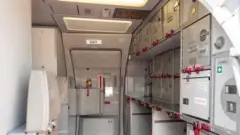 A cozinha de um avião com armários de armazenamento e uma saída de emergência