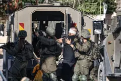 جنود من الجيش الإسرائيلي يعتقلون رجلاً معصوب العينين ويسحبونه إلى سيارة مصفحة.