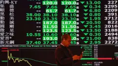 Мужчина делает селфи с экранами, показывающими падение стоимости акций на Тайваньской фондовой бирже