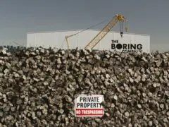 Uma vista do prédio da Boring Company com uma parede em primeiro plano, incluindo uma placa que diz "propriedade privada, entrada proibida"