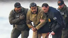 Maduro, com olhar apreensivo e em pé, é escoltado por agentes americanos