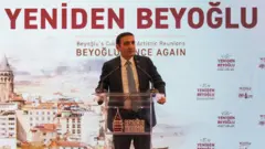 İnan Güney, arka planında "Yeniden Beyoğlu" yazan bir sahnede bulunan kürsüde konuşma yaparken