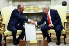 Sentados, o presidente americano Donald Trump e o chanceler alemão Friedrich Merz se cumprimentam com um aperto de mão na Casa Branca