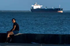 Una mujer sentada en el malecón del lago de Maracaibo ya lo lejos un tanque de petróleo.