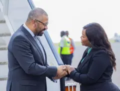 Minisitiri w'ubutegetsi bw'igihugu w'Ubwongereza James Cleverly (ibumoso) asuhuzanya n'umunyamabanga uhoraho muri minisiteri y'ububanyi n'amahanga y'u Rwanda Clémentine Mukeka, ku kibuga mpuzamahanga cy'indege cya Kigali, ku itariki ya 5 Ukuboza (12) mu 2023