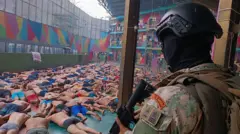 Un militar encapuchado ecuatoriano vigila a un montón de presos acostados boca abajo con el torso desnudo en la Penitenciaría del Litoral, en Guayaquil.