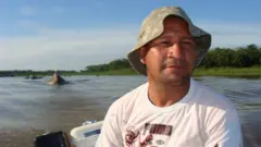 O manejador Pedro Canízio em um barco, com camiseta da maca Puma e um chapéu de pescador
