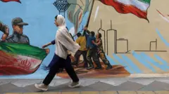 An Iranian woman walks next to a mural on a street in Tehran
