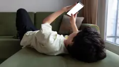 Bir çocuk elinde telefon yatıyor ve ekrana bakıyor