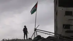 Homem com jaleco olha para um edifício destruído na Faixa de Gaza