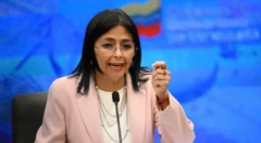 Vice-presidente da Venezuela, Delcy Rodríguez fala ao microfone, usa terno rosa e o fundo da imagem é azul