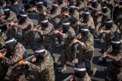 Vários membros do IRGC em roupas militares e balaclavas pretas apontam suas armas durante um exercício.