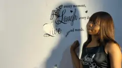 Sade (wanda ba shi ne sunanta na asali ba) tsaye a gaban wani bango a ɗakinta a Legas