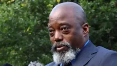 Ifoto Joseph Kabila yafotowe yegerewe, yiyogosheje amaraho umusatsi mu mutwe, afite n'ubwanwa burebure burimo n'imvi, yambaye ikositimu yijimye. Yari arimo kuvugira i Johannesburg, muri Afurika y'Epfo, ku itariki ya 18 Werurwe (3) mu mwaka wa 2025. 