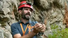 Homem branco de cabelo preto com equipamentos de exploração de caverna
