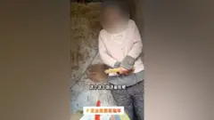 A screenshot from the video shows the woman with a chain around her neck