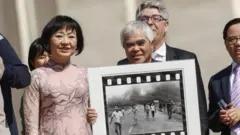Nick Ut com Kim Phuc. O fotógrafo mostra a icônica foto da Guerra do Vietnã enquanto aguardam o encontro com o Papa Francisco no final de sua audiência geral semanal na Praça de São Pedro, Cidade do Vaticano, em 11 de maio de 2022.
