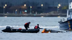 Rescue teams in a rib on the Hudson river grab onto the underside of the helicopter just visible above the water line, in New York on Thursday