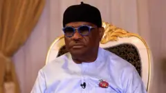 Nyesom Wike sitdown for chair wit strong face, e wear black cap blue eyeglass and armed forces badge.