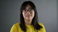 黄色い服を着て眼鏡をかけた髪の長い人がほほ笑んでいる