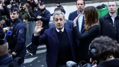 Sarkozy levanta la mano rodeado de miembros de las fuerzas de seguriidad y de su esposa. 