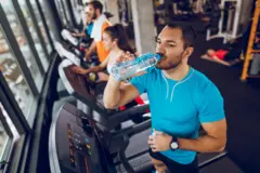 Varias personas haciendo ejercicio en un gimnasio donde un hombre bebe agua.