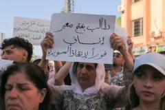 إمرأة درزية ترفع لافتة كتب عليها "نطالب بفتح معبر إنساني فورا لإنقاذ السويداء" وتحيط بها عدة سيدات خلال تظاهرة من أجل تحسين الأوضاع بالمدينة في يوليو الماضي.