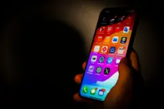 Bir kişi elinde cep telefonu tutuyor. Telefonda uygulamalar görülüyor.