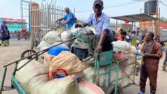 Musa Waseme yicaye ku igare ritwara ibicuruzwa agiye kugurisha hakurya i Goma