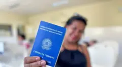 Mulher desfocada segurando uma carteira de trabalho, que aparece em primeiro plano e em foco