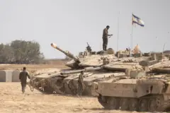 يظهر اثنان من الجنود الإسرائيليين قرب دباباتهم وآخر يقف على ظهر إحدى الدبابات. وعلى ظهر دبابة العلم الإسرائيلي. المنطقة ترابية قريب منها عدد قليل من الأشجار. الصورة التقطت نهاراً.