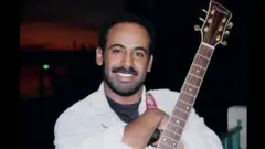 ኣብርሃም ኣፈወርቂ ጊትራ ሒዙ ፍሽኽ ኢሉ ናብ ካሜራ እናጠመተ