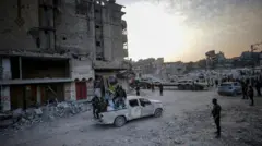 Milicianos de Hamás sentados en la parte trasera de una camioneta, entre edificios destruidos en Ciudad de Gaza.