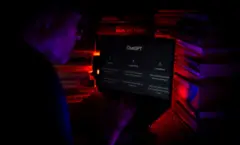 Um homem usando o computador na aba do ChatGPT. Ele está no escuro
