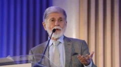 Foto mostra Celso Amorim, homem branco, de cabelos e barba brancas, usando terno cinza em um púlpito falando ao microfone