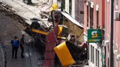 два человека стоят рядом с упавшей кабинкой фуникулера в лиссабоне