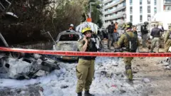 Equipes de emergência israelenses trabalham no local de um ataque de míssil iraniano em uma área residencial de Tel Aviv, Israel, em 24 de março de 2026.